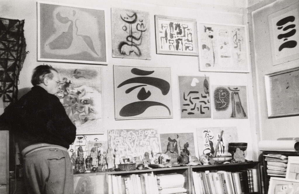 Willi Baumeister vor Wand mit Bildern aus der eigenen Sammlung