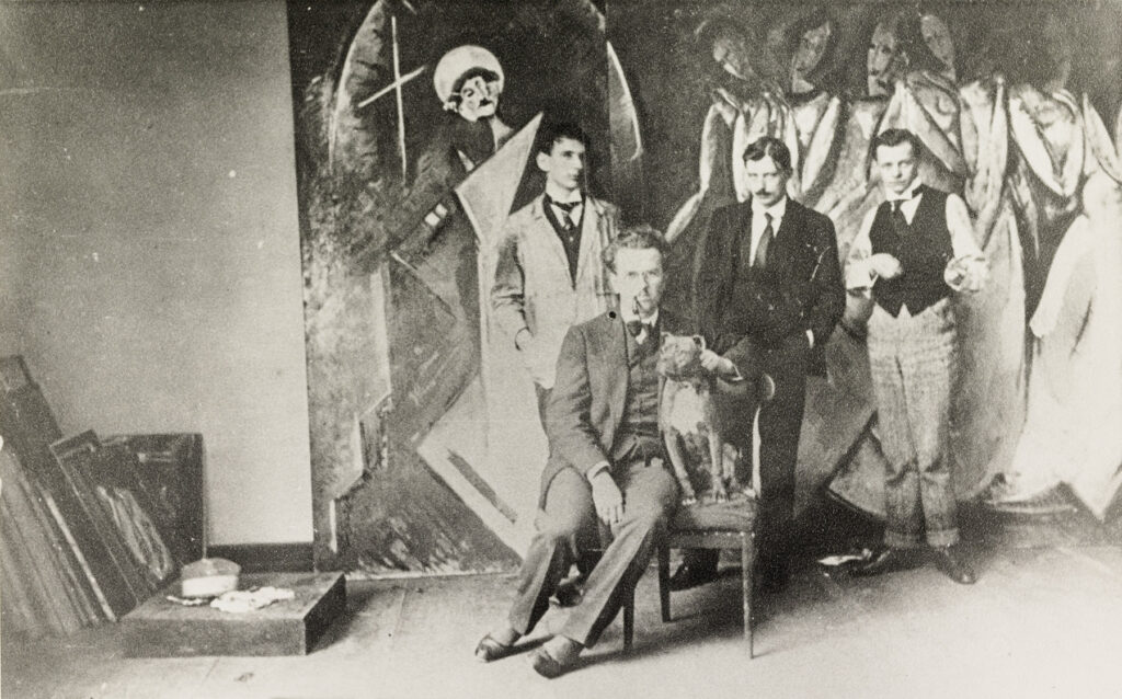 Foto: schwarz-weiß: Hermann Stenner, Karl Bürckle, Oskar Schlemmer und sitzend: Edmund Daniel Kinzinger vor Schlemmers Wandbild "Wunder der weißen Nonne" für die Kölner Werkbund-Ausstellung 1914