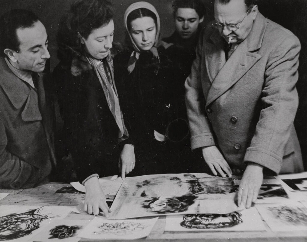 Willi Baumeister zeigt etwas anhand von Zeichnungen den anderen Personen auf dem Foto