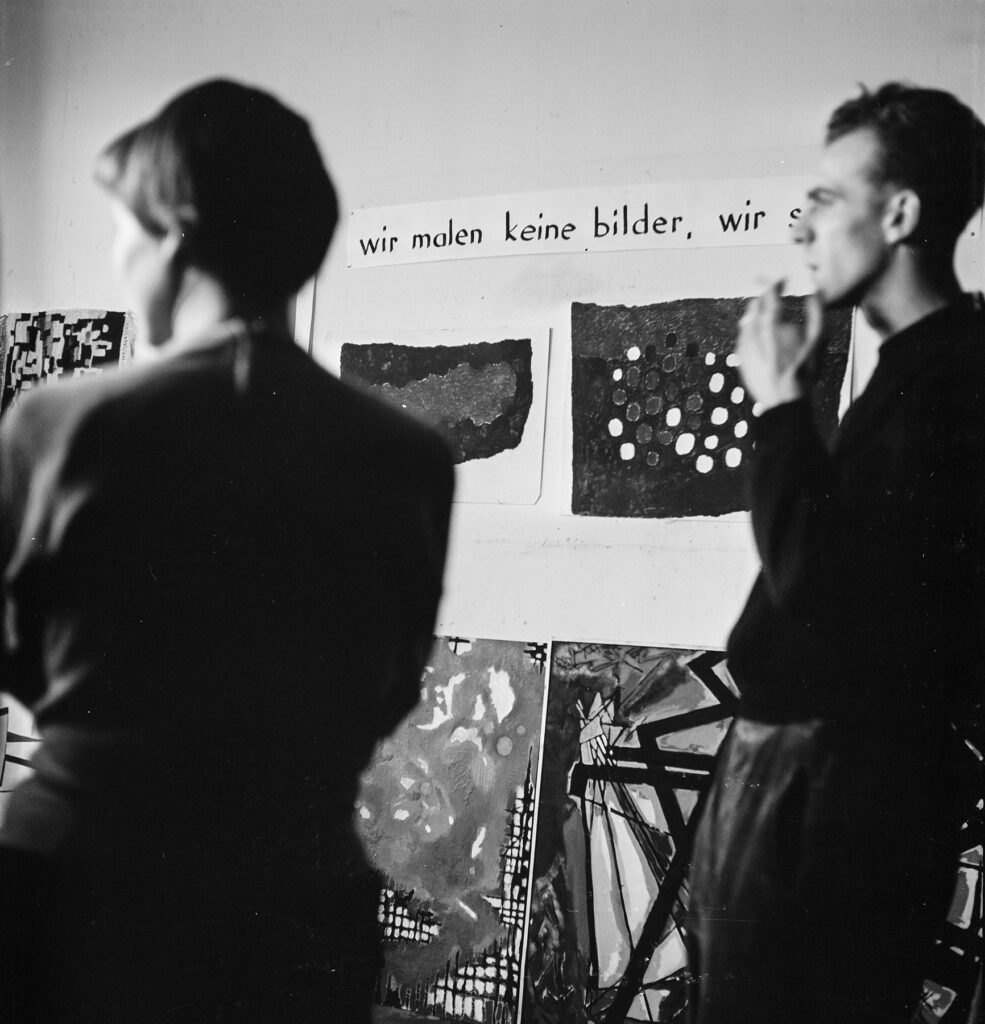 Foto: schwarz-weiß: Wand mit Bildern und mit dem Satz "wir malen keine bilder, wir studieren"