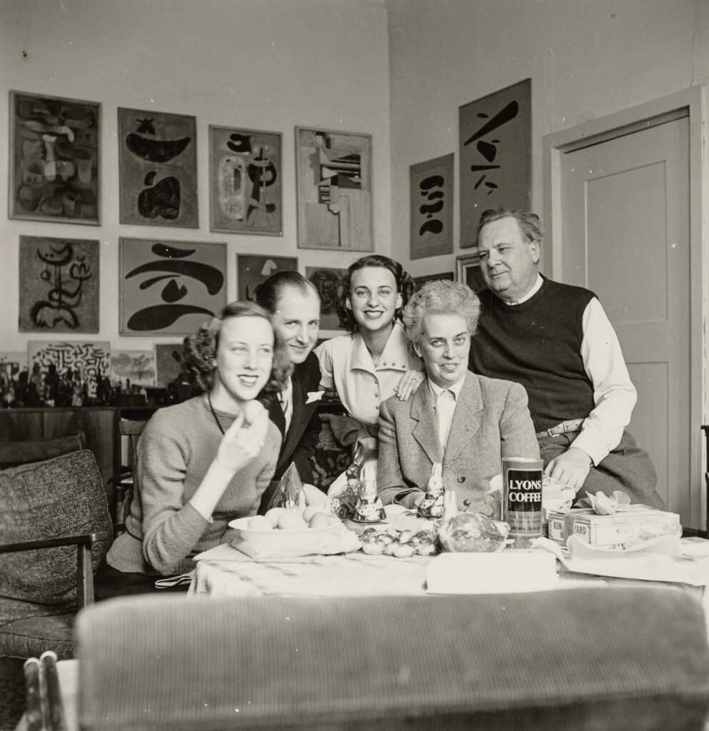Familie Baumeister mit Besuch an Ostern um einen Tisch