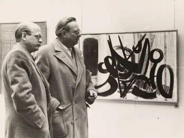 WILLI BAUMEISTER - EIN FILM VON OTTOMAR DOMNICK
1954 fand die Uraufführung des Films >Willi Baumeister< von Regisseur Ottomar Domnick in Amsterdam statt. Er lief erfolgreich auf verschiedenen Filmfestivals und erhielt mehrere Auszeichnungen. Der Film wurde in verschiedene Sprachen synchronisiert. Baumeister selbst nannte ihn den „wahrscheinlich besten Künstlerfilm bis heute.“ In den letzten Jahrzehnten wurde der Kulturfilm jedoch nur selten gezeigt - zumeist bei ausstellungsbegleitenden Veranstaltungen.

Die abstrakte Kunst, die noch in den 1950er Jahren bei vielen Zeitgenossen zu Kopfschütteln führte, begeisterte den Filmautor Ottomar Domnick. Er brannte für die Idee, die neue Kunst verständlicher zu machen. Der Kunstfilm zeigt den Künstler Willi Baumeister in seinem Atelier und bei seiner Arbeit. In knapp 30 Minuten führt er in dessen Bilderwelt ein und zeigt darüber hinaus in seiner kurzen Sequenz szenische Aufnahmen einer von Baumeister ausgestatteten Theateraufführung. Domnick arbeitet mit assoziativen Bildvergleichen, erklärt mit Trickfilm-Sequenzen, raffinierten Überblendungen und Aufhellungen den Aufbau eines Gemäldes und unterstreicht die Modernität durch die musikalische Untermalung mit einem Elektronium - einer instrumentalen Neukonstruktion.

Mehr Information im ausführlichen Booklet zur DVD, die zum 60. Todestag von Willi Baumeister (1889-1955) in Zusammenarbeit mit dem Archiv Baumeister @kunstmuseumstuttgart , der Stiftung Domnick und der Willi Baumeister Stiftung erschienen ist.
https://willi-baumeister.org/meldungen/e-book/

📸 Ottomar Domnick und Willi Baumeister vor einem Gämelde von Hans Hartung (Ausstellung zum Künstler „Hans Hartung und die deutsch-französische Freundschaft“ aktuell @predigermuseum in Schwäbisch Gmünd zu sehen), Stuttgart, 1948. Foto: M. Winkler-Betzendahl.
#willibaumeisterstiftung#stiftungdomnick#kunstmuseumstuttgart#hanshartung#predigermuseum
